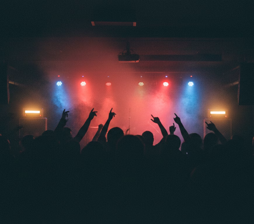 Ilustrație AI: public dintr-un club rock underground, văzut din spate, în fum și lumini roșii și albastre
